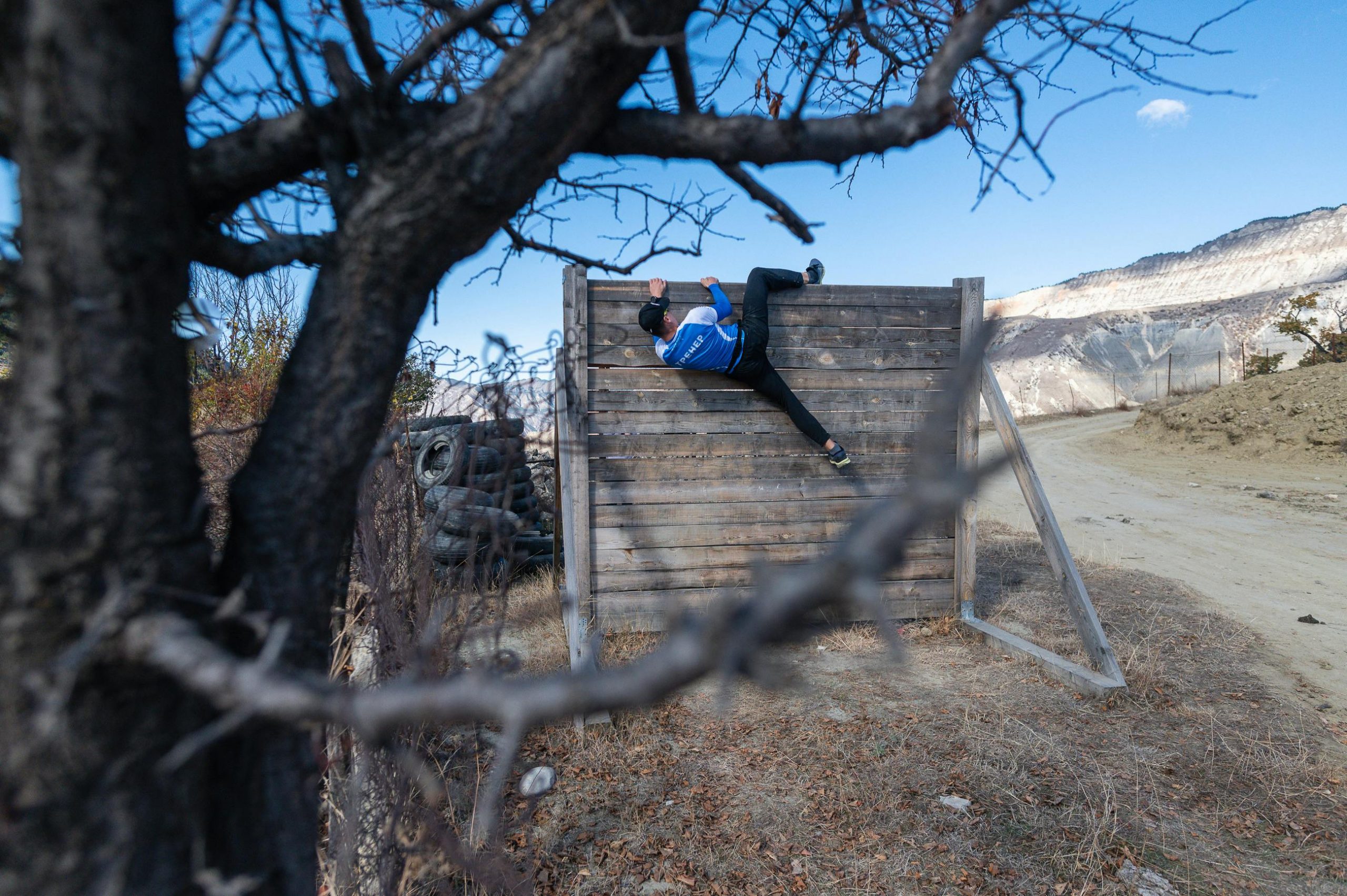 Adult man climbing a wooden wall in an outdoor obstacle course during fall.
