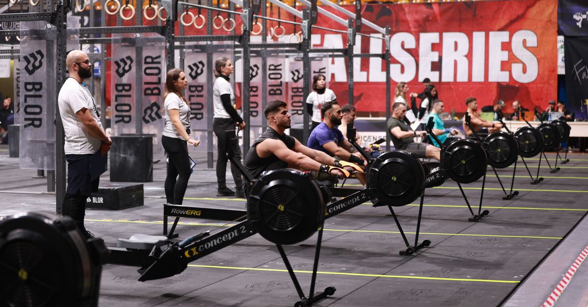 Competitors row on machines during an indoor fitness event. Focus on teamwork and endurance.
