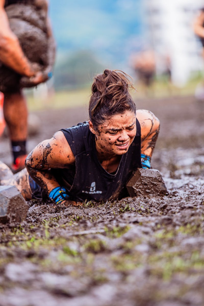 Determined woman crawling through muddy ground in challenging obstacle race.