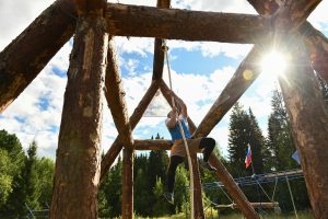 Adult man climbs rope on a wooden obstacle structure during a sunny day.
